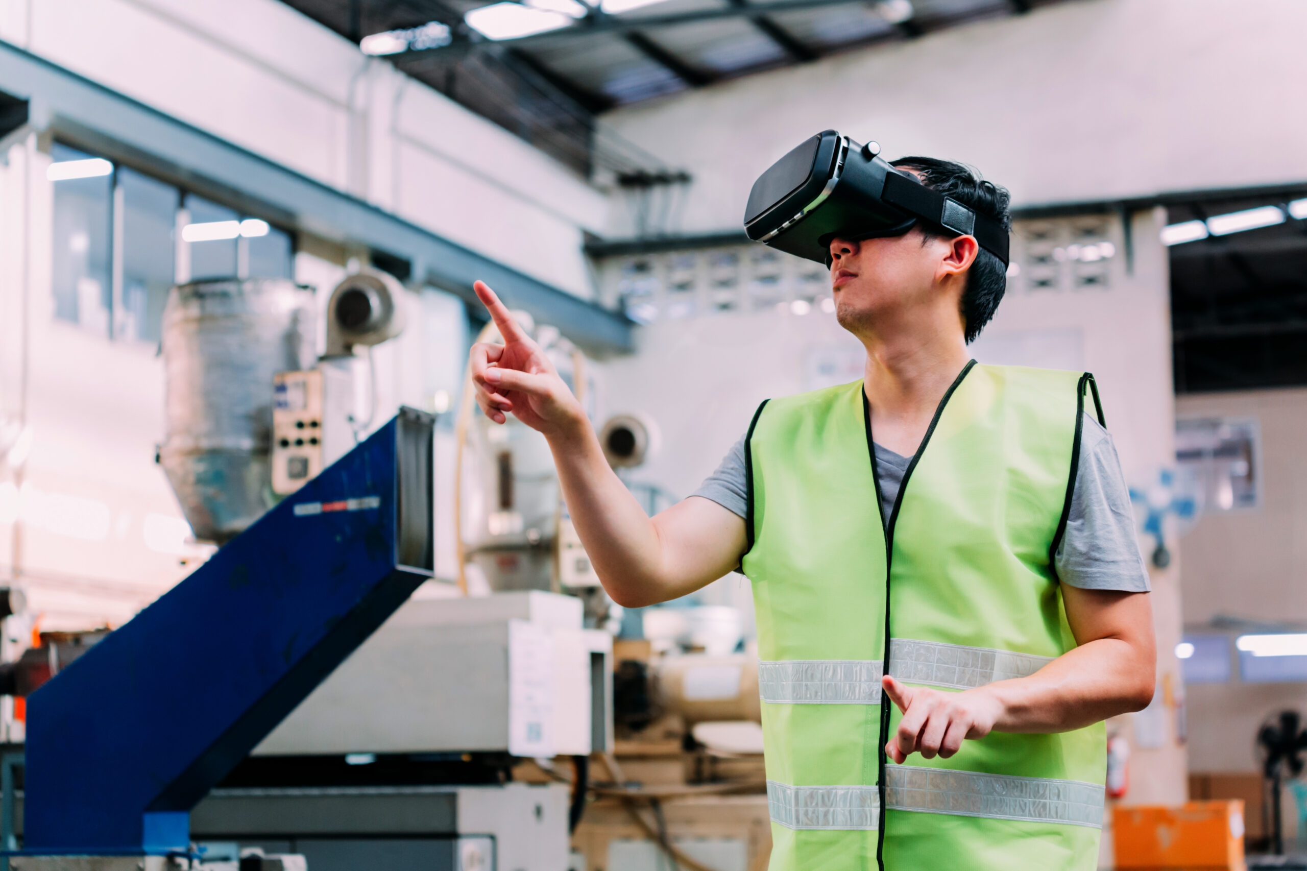 Industrial factory and manufacturing engineering worker wearing VR goggle headset touching in virtual reality simulation alongside heavy duty machines